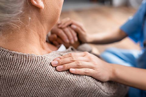 massage therapist hands on shoulder elderly homebound patient